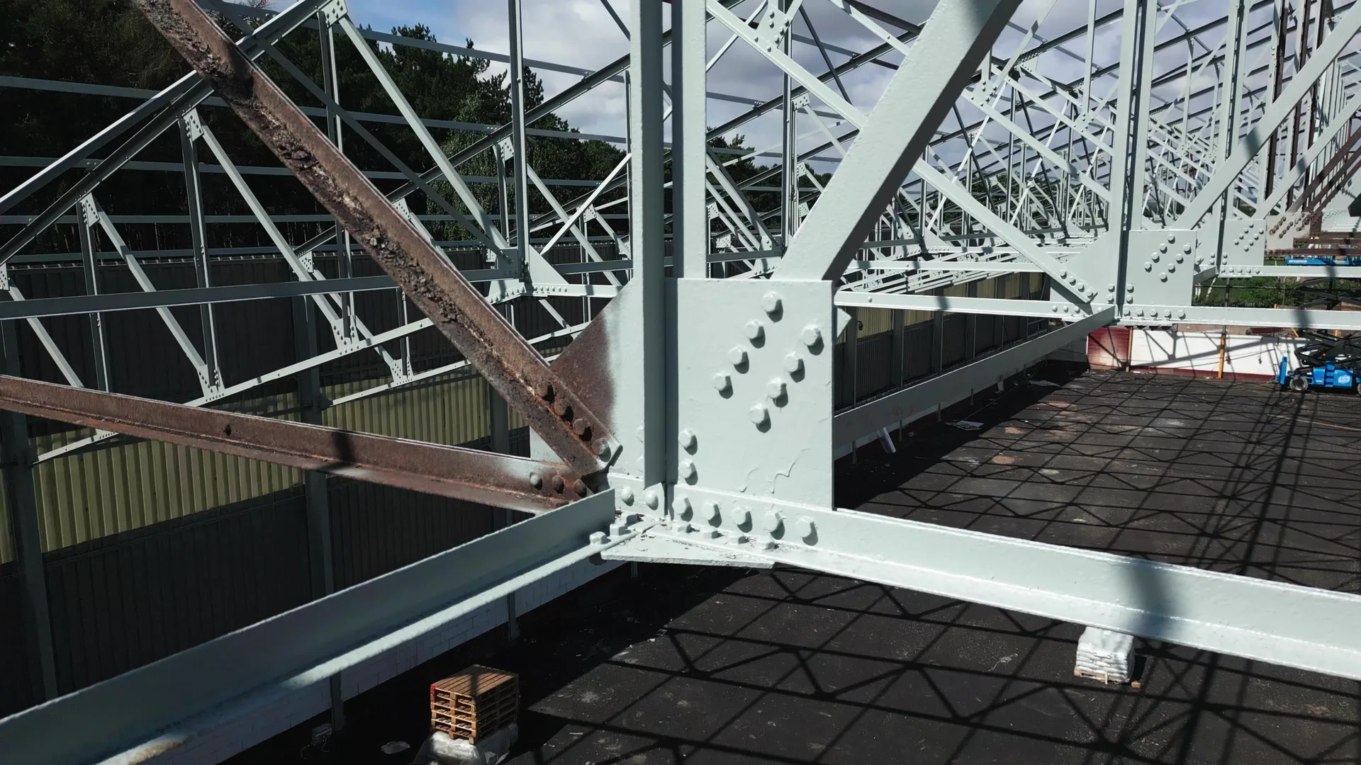 Red powered access platform positioned beneath a structural steel frame during coating work.