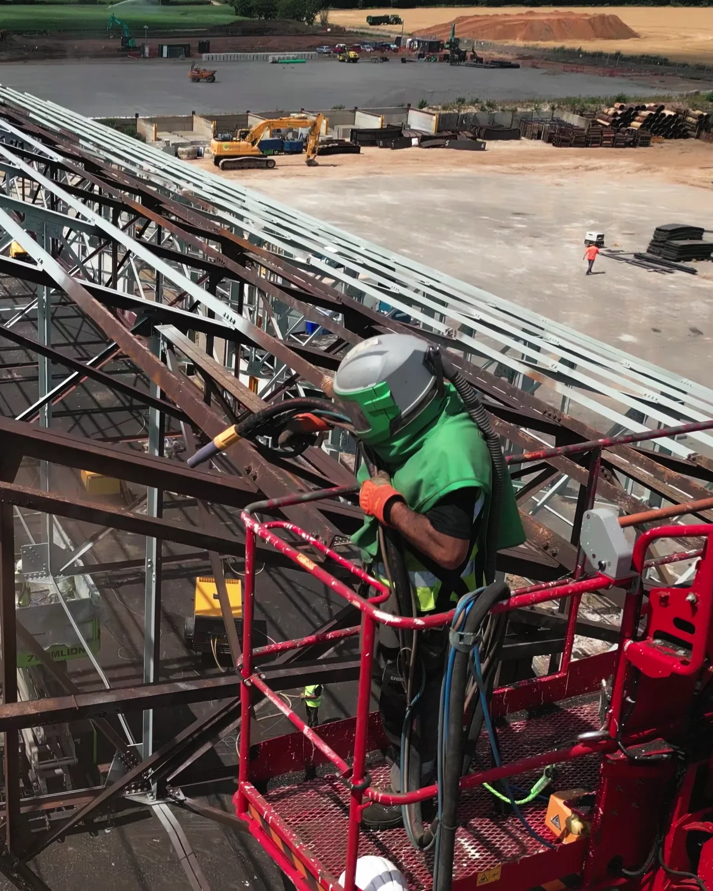 Portrait view of a coating operative positioned beside structural steel from powered access equipment.