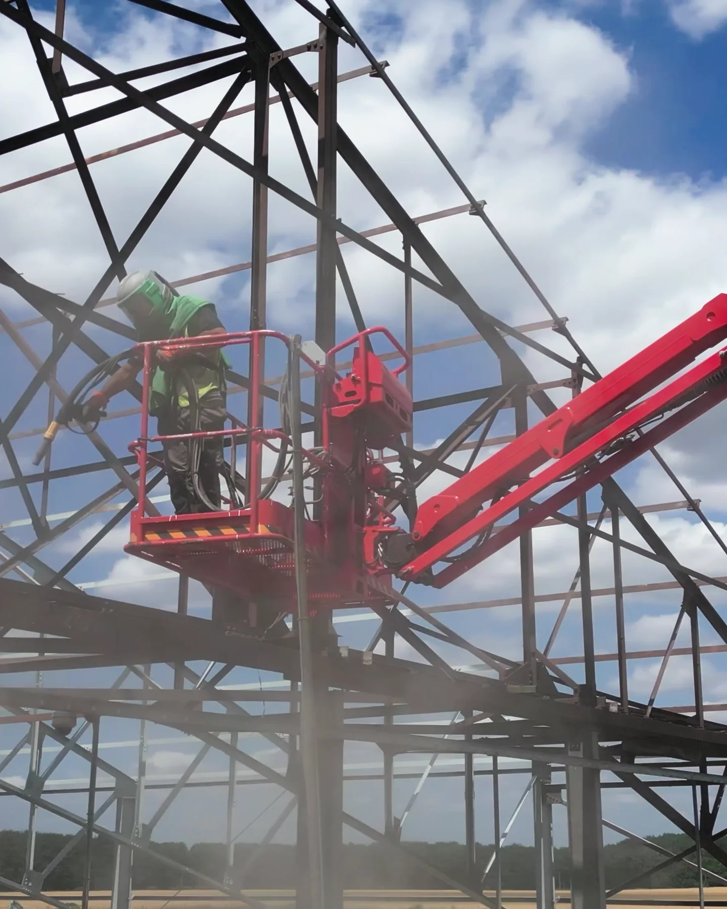 Portrait crop of powered access beneath a structural steel frame during a coating project.
