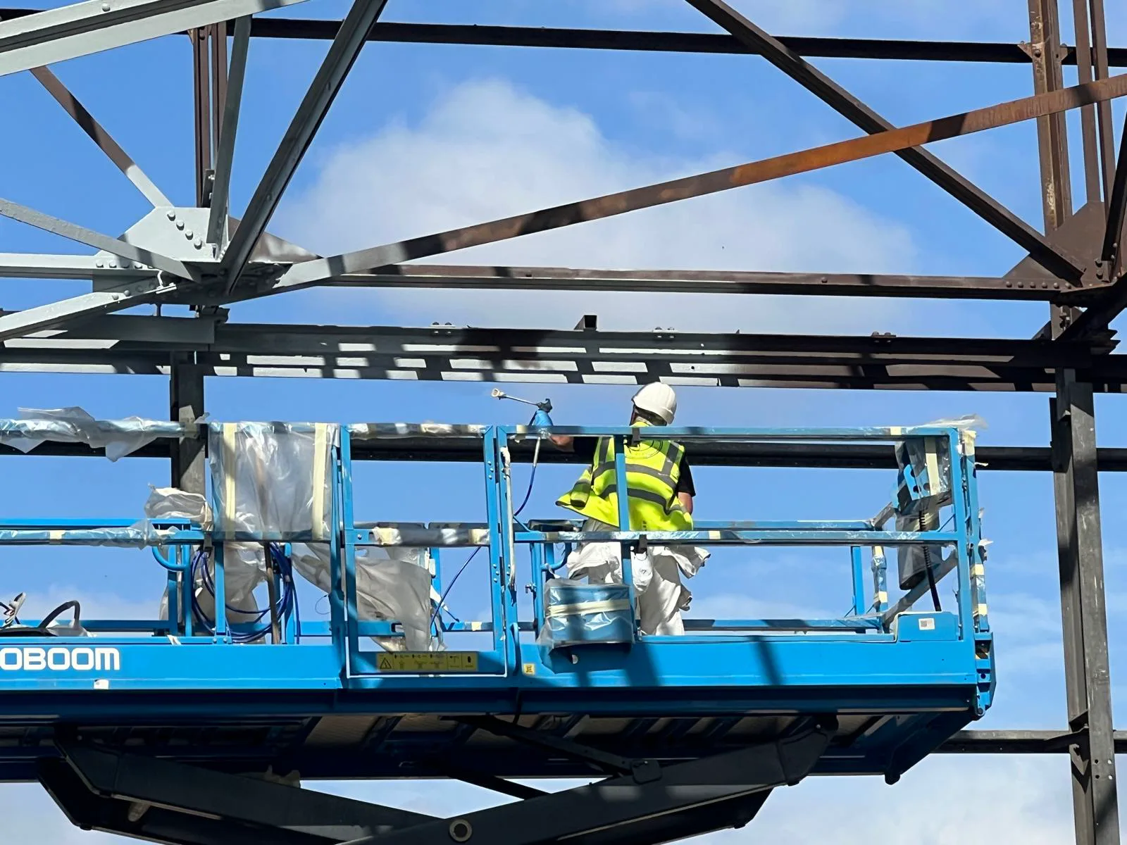 Wide view of a Premier Blasting operative coating structural steel from powered access equipment